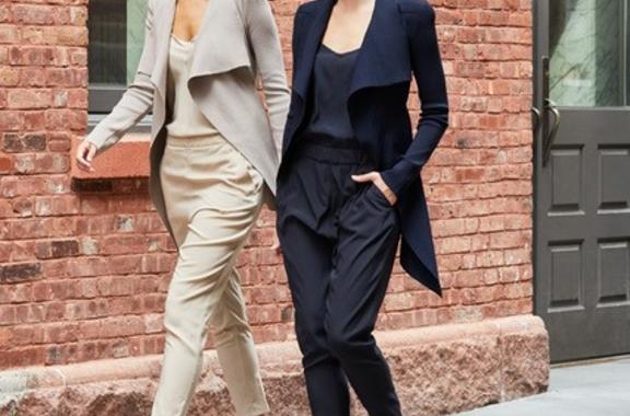 two women walking in silk pants and jackets one beige and one black 