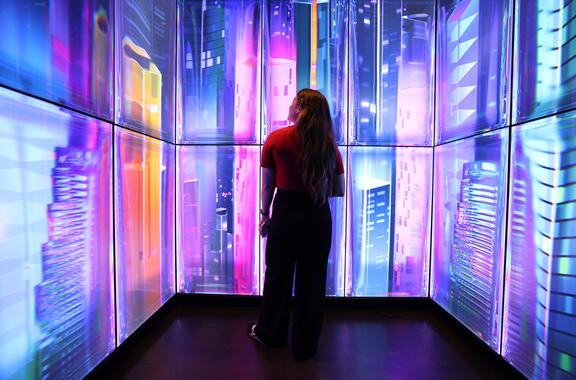 women standing in elevator with screen illuminated but a cityscape